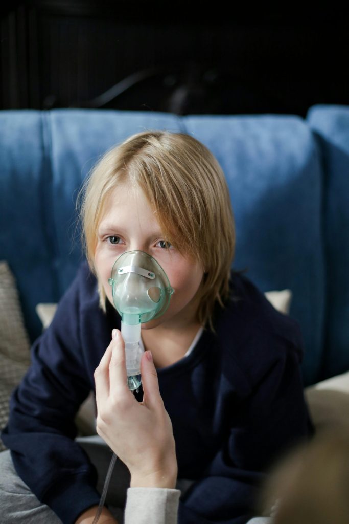 Ein Kleinkind sitzt auf einem Sofa und erhält drinnen eine Inhalationstherapie.