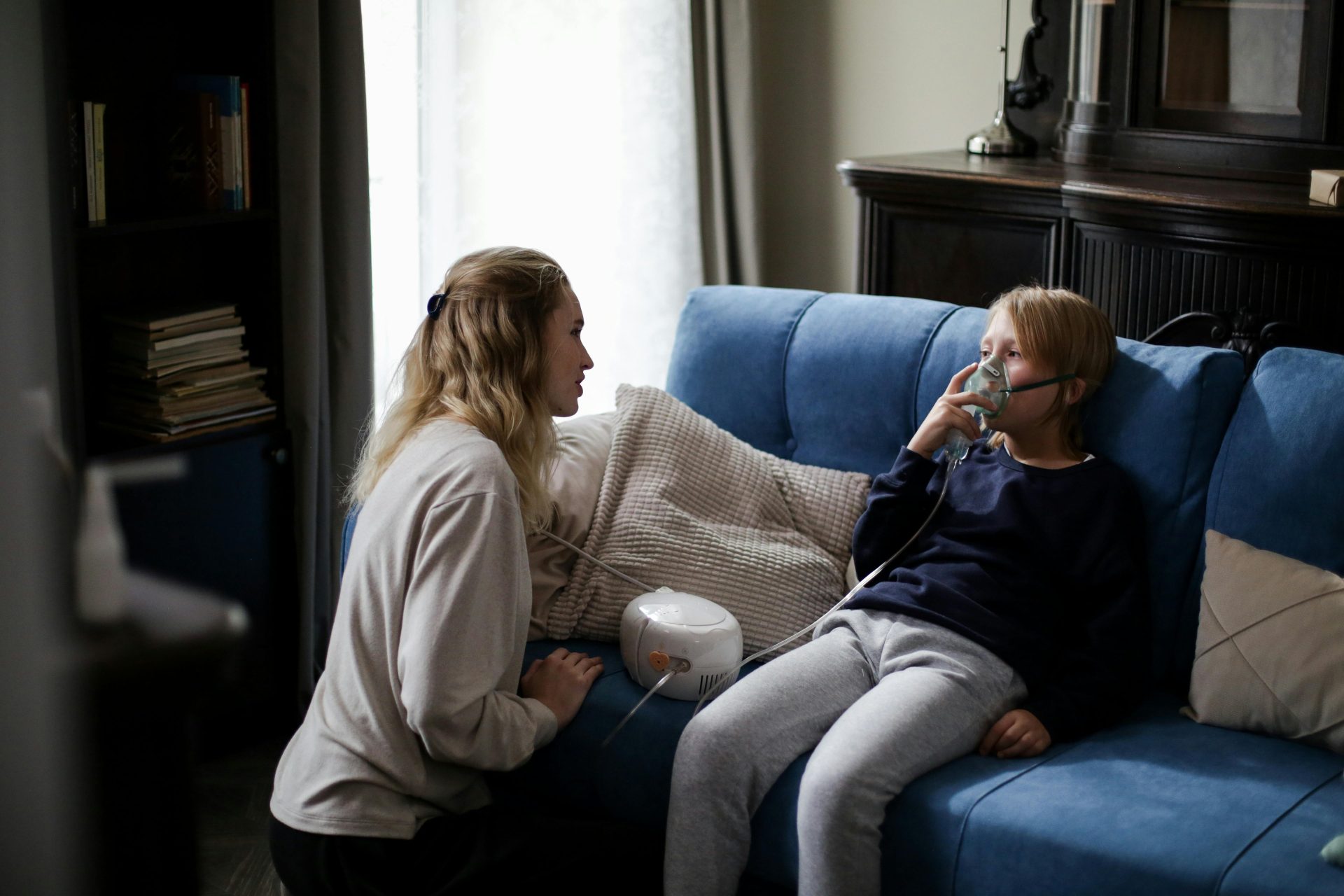 Eine Mutter unterstützt ihr krankes Kind zu Hause bei der Anwendung eines Verneblers und spendet ihm dabei Trost und Fürsorge.